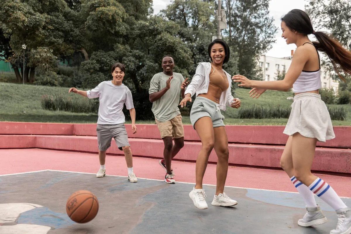 Group of friends playing basketball on an outdoor court, smiling and enjoying the game.