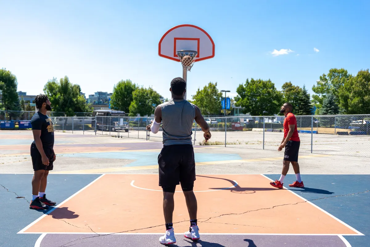Three players on an outdoor basketball court practicing shooting.