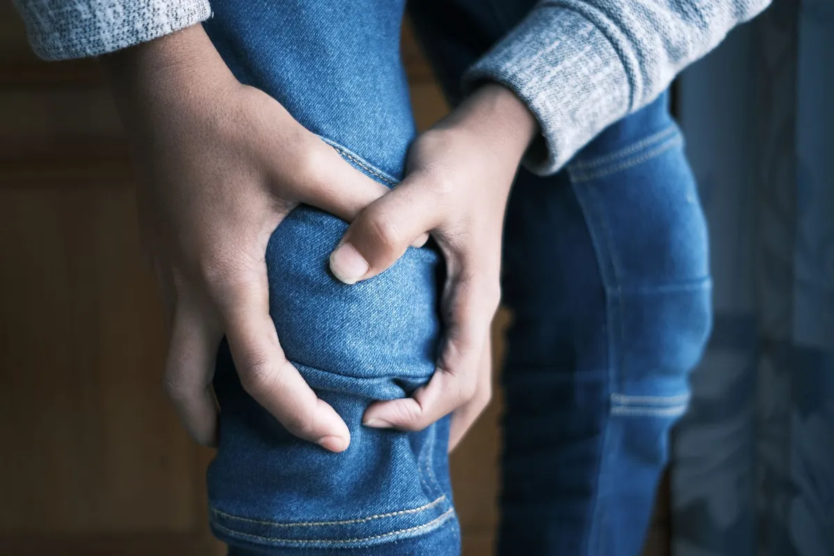 Person holding their knee in pain, indicating a possible injury.