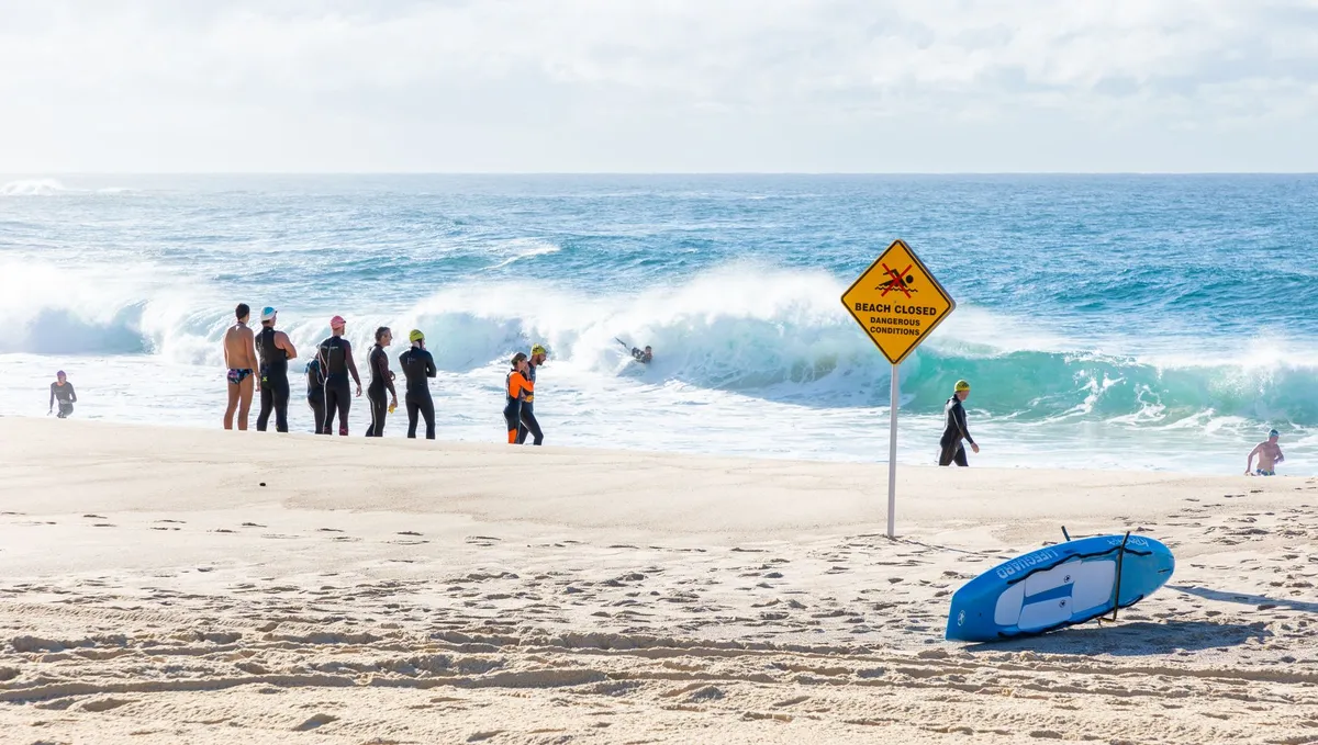 Beach closed sign with people near the water and waves crashing in the background.