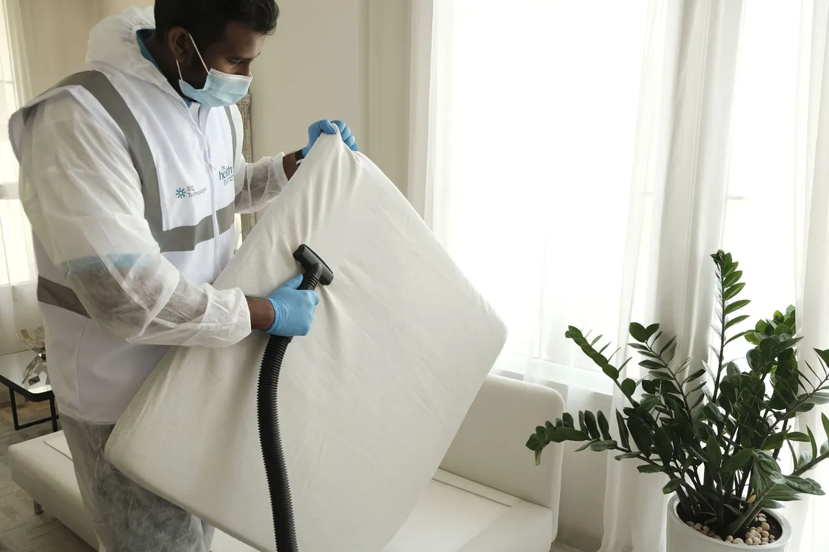 Person inspecting a mattress with a vacuum for bedbugs in a bright room.