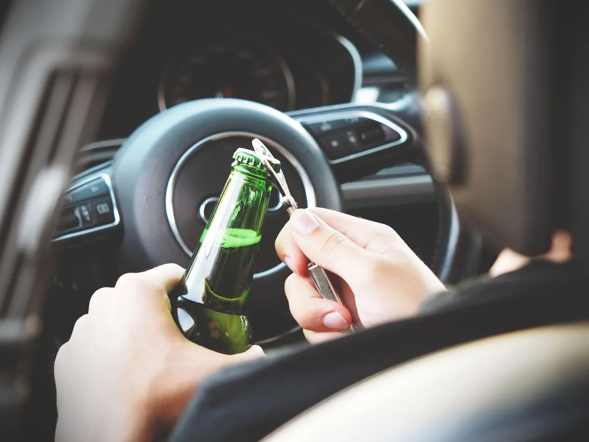 Hands holding a beer bottle while seated in a car, indicating potential binge drinking.