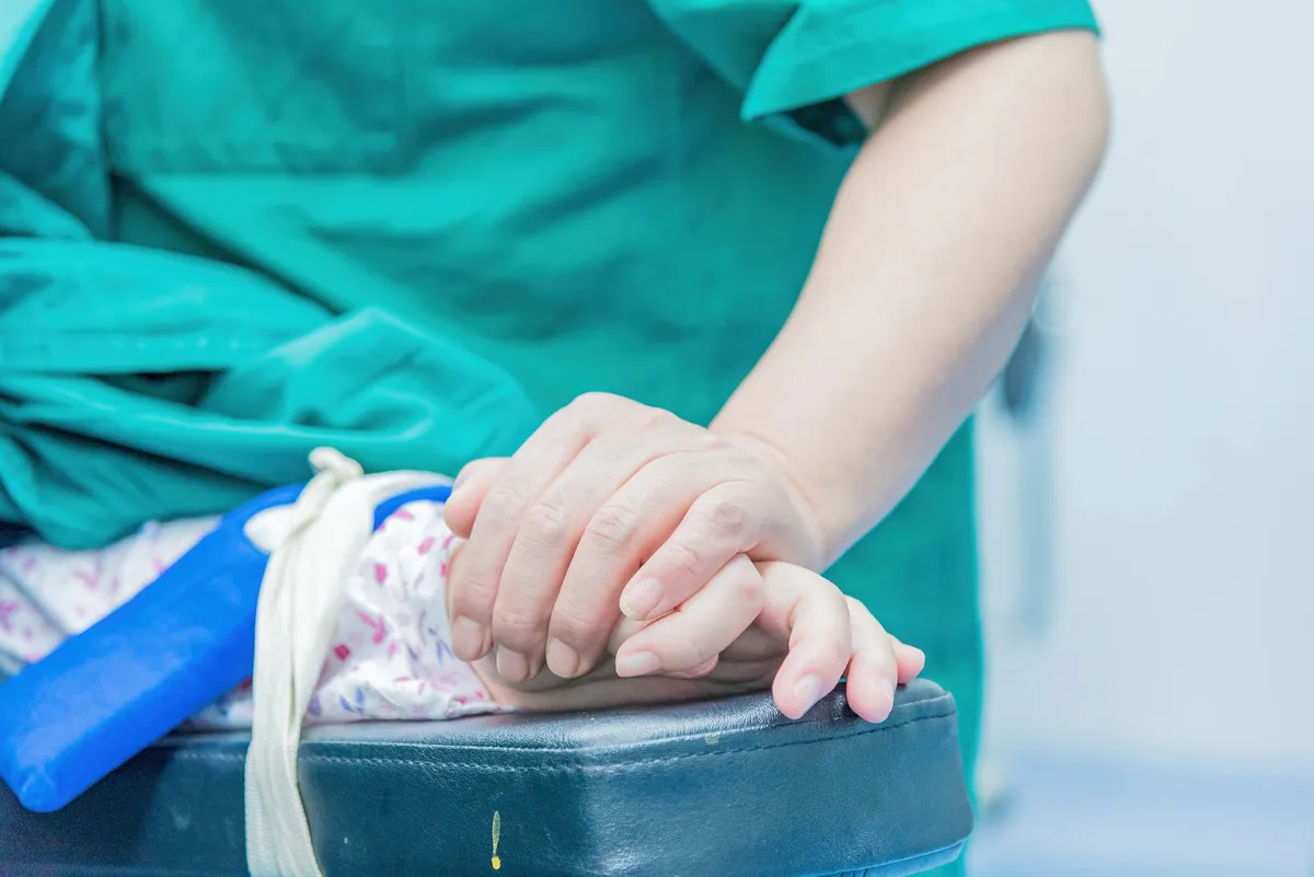 A healthcare professional holds a patient’s hand for support before a procedure.