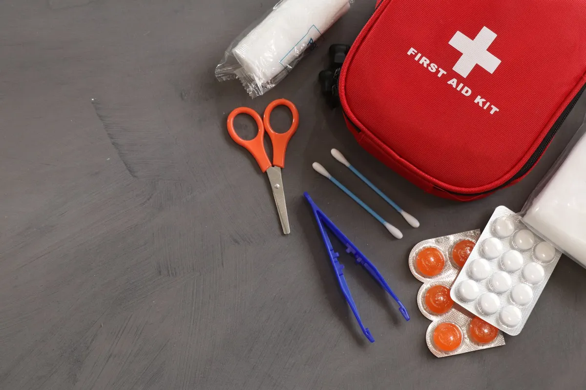 Red first aid kit with scissors, bandages, and cotton swabs on a surface.