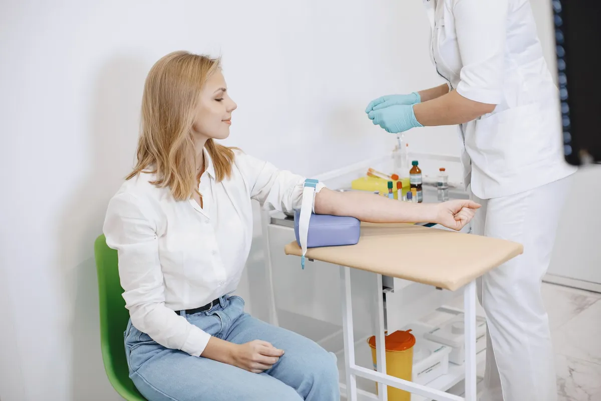 A woman sitting in a clinical setting receiving a blood draw.