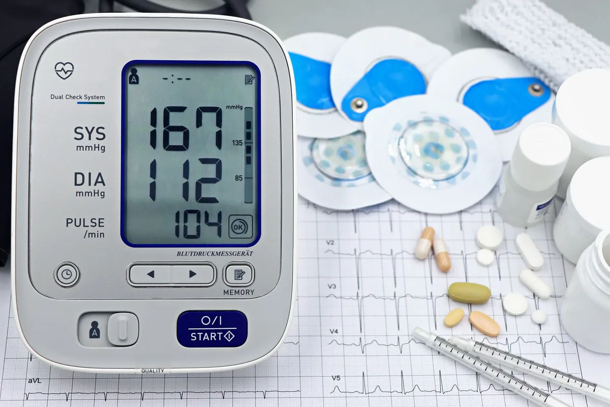 Blood pressure monitor displaying high readings with medication and charts nearby.