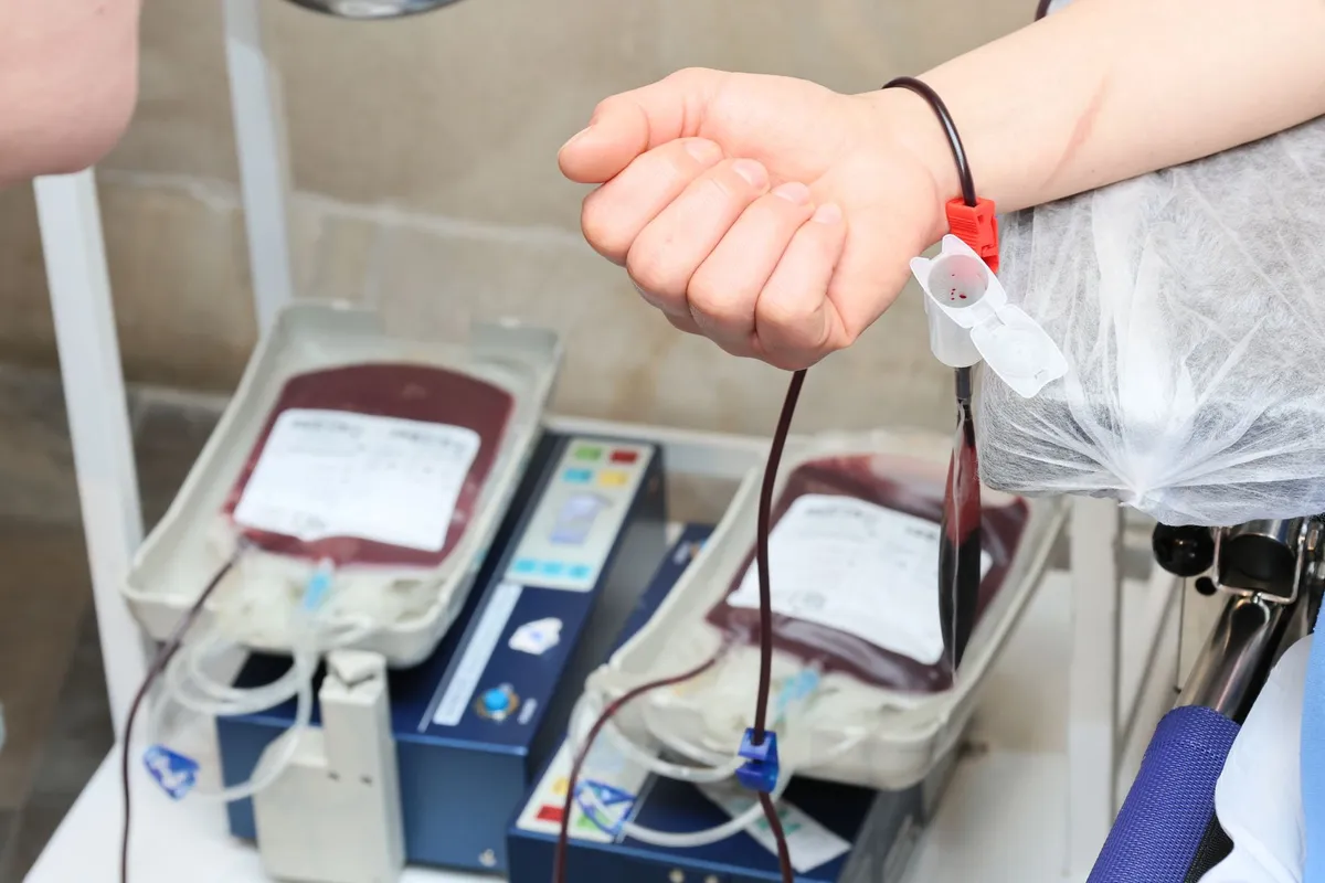 Patient’s arm with blood transfusion setup and blood bags visible.