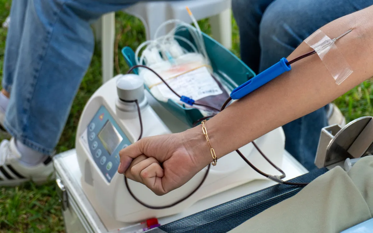 Arm with a needle for blood donation connected to a machine.