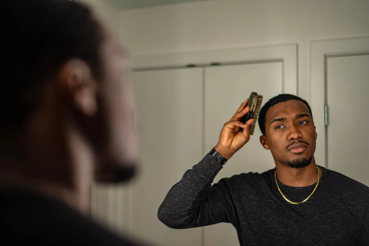 Man grooming himself while looking in the mirror, reflecting on body image.
