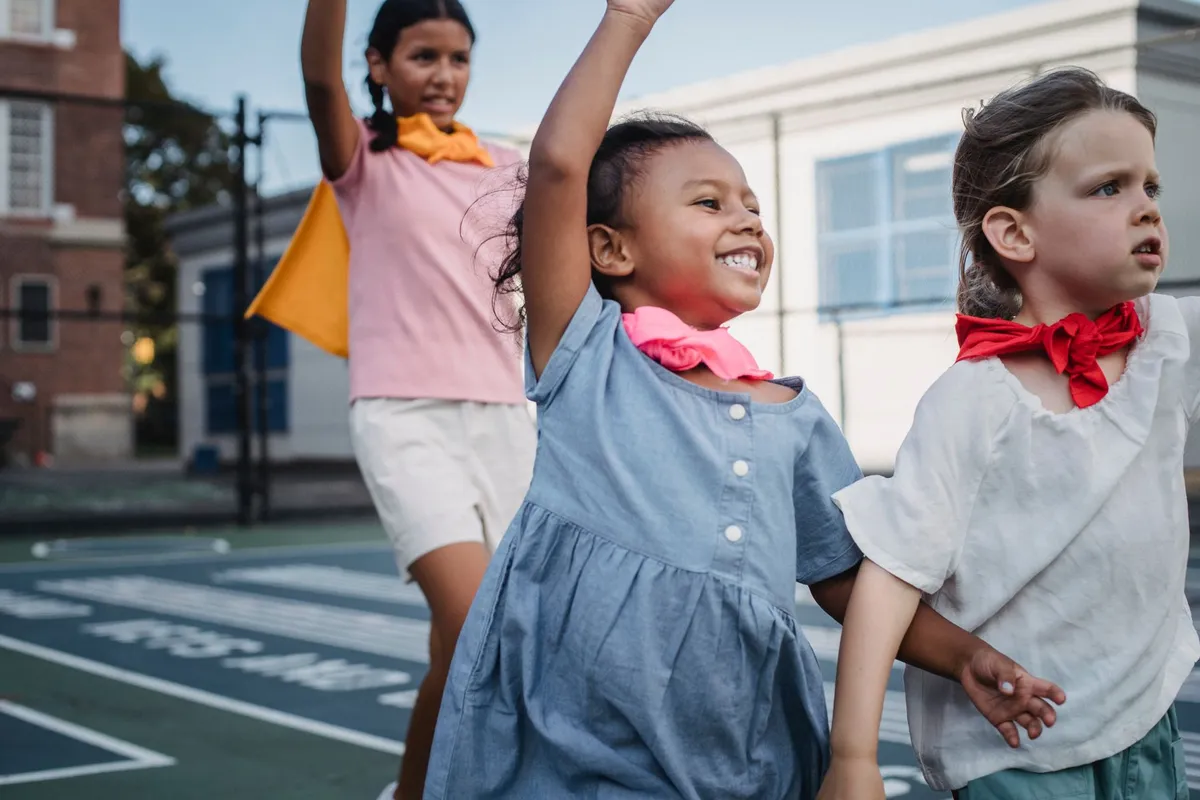 Children playing and smiling outdoors in colorful capes during a fun activity.