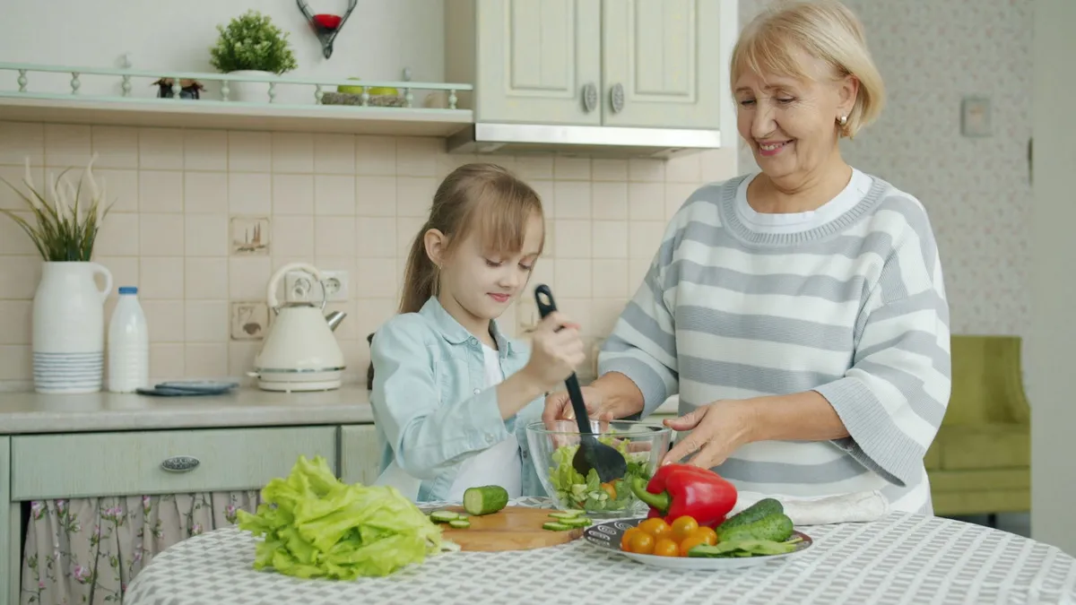 Grandmother and granddaughter preparing a salad together in a kitchen.