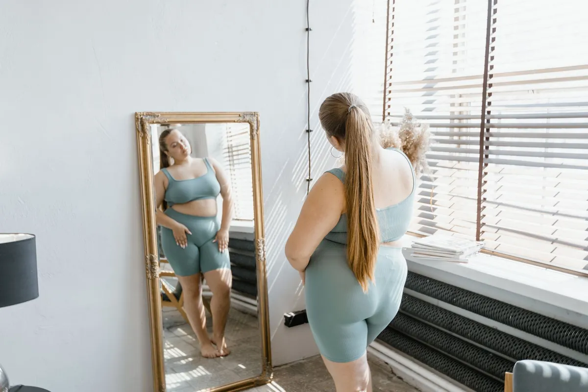 Woman in activewear looking at her reflection in a full-length mirror.