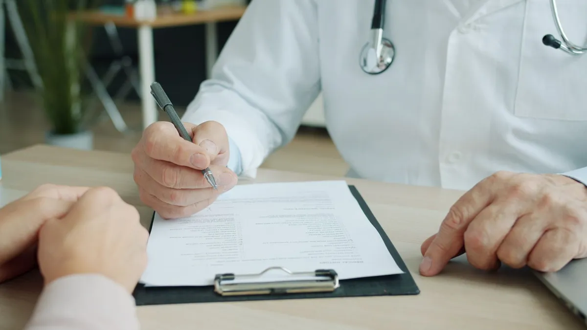Doctor’s hands writing notes while consulting with a patient about health issues.