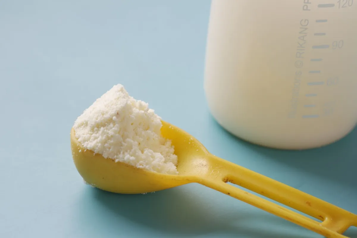 Close-up of a yellow scoop filled with infant formula next to a baby bottle.