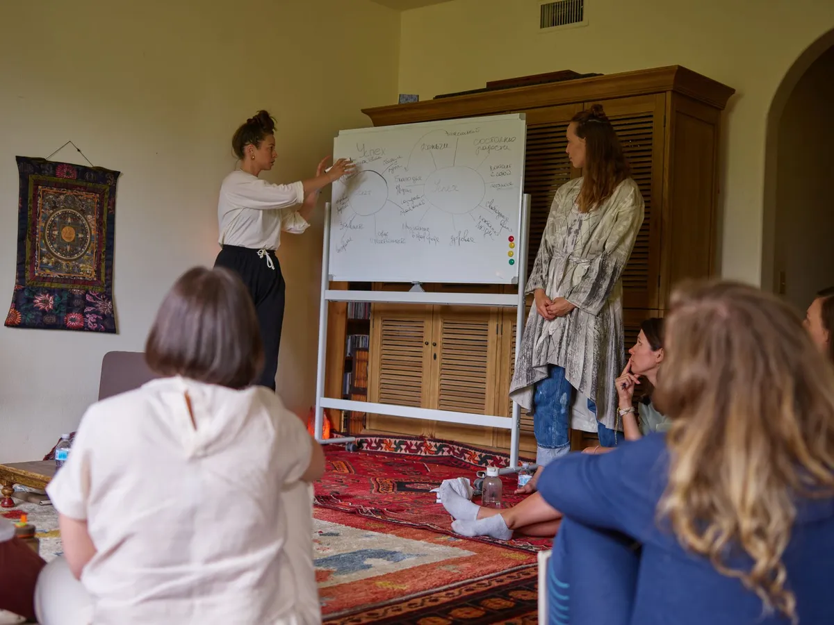 Two women presenting in a workshop setting with participants seated on the floor.