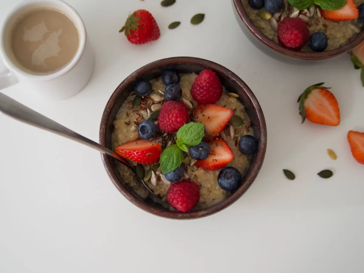 Bowl of oatmeal topped with strawberries, raspberries, blueberries, and seeds.