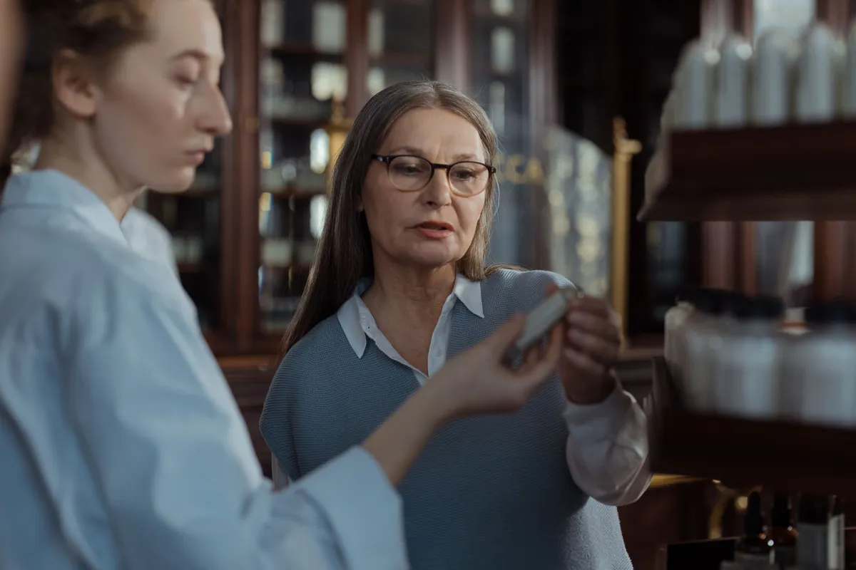 Pharmacist showing medication to an older woman in a pharmacy setting.