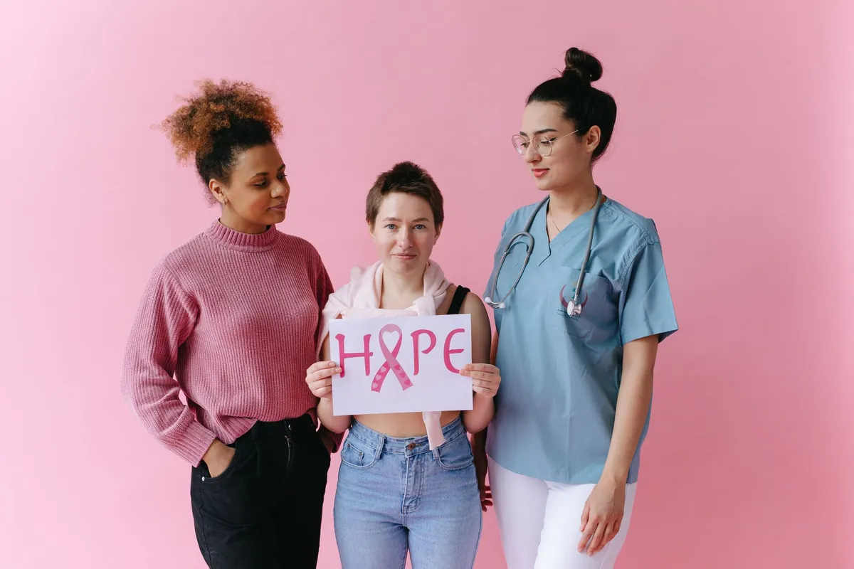 Three women holding a sign that says ‘HOPE’ with a pink ribbon, symbolizing breast cancer awareness.