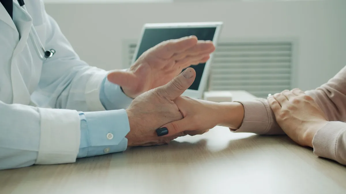 A healthcare provider discussing with a patient, hands on a table.