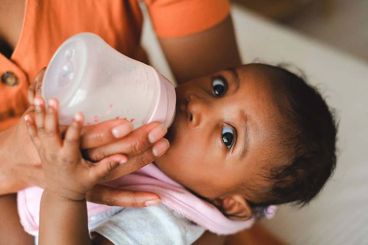 Baby feeding from a bottle held by an adult, showing close-up of the baby’s face.