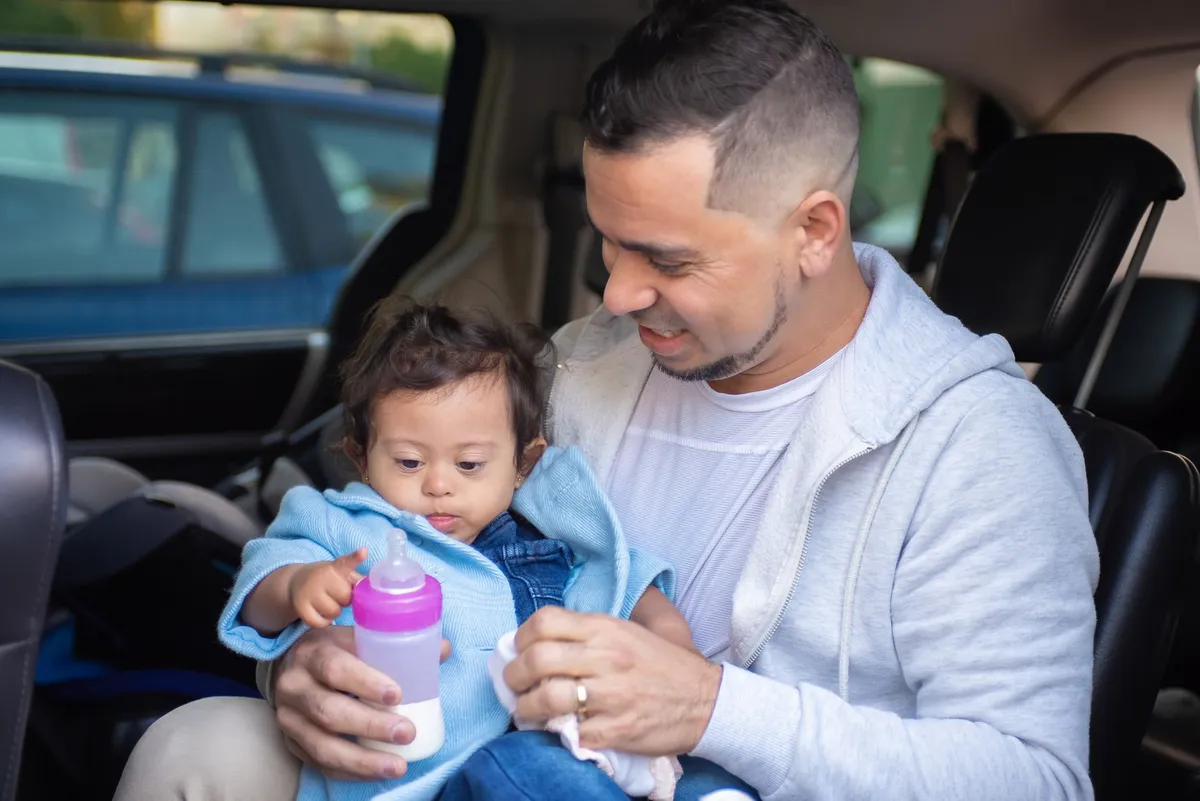 Parent feeding a baby in a car with a bottle.