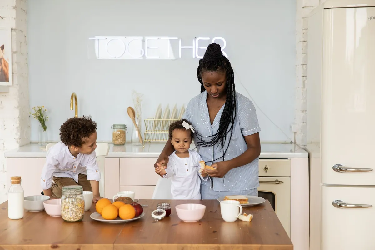 A mother and two children preparing a healthy breakfast with fruits and yogurt in a kitchen.