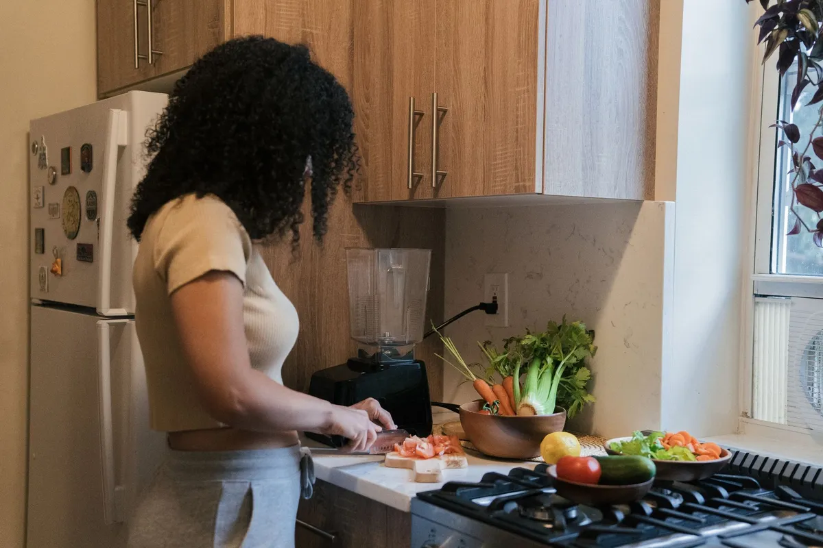 Woman chopping vegetables in a kitchen with fresh produce on the counter.