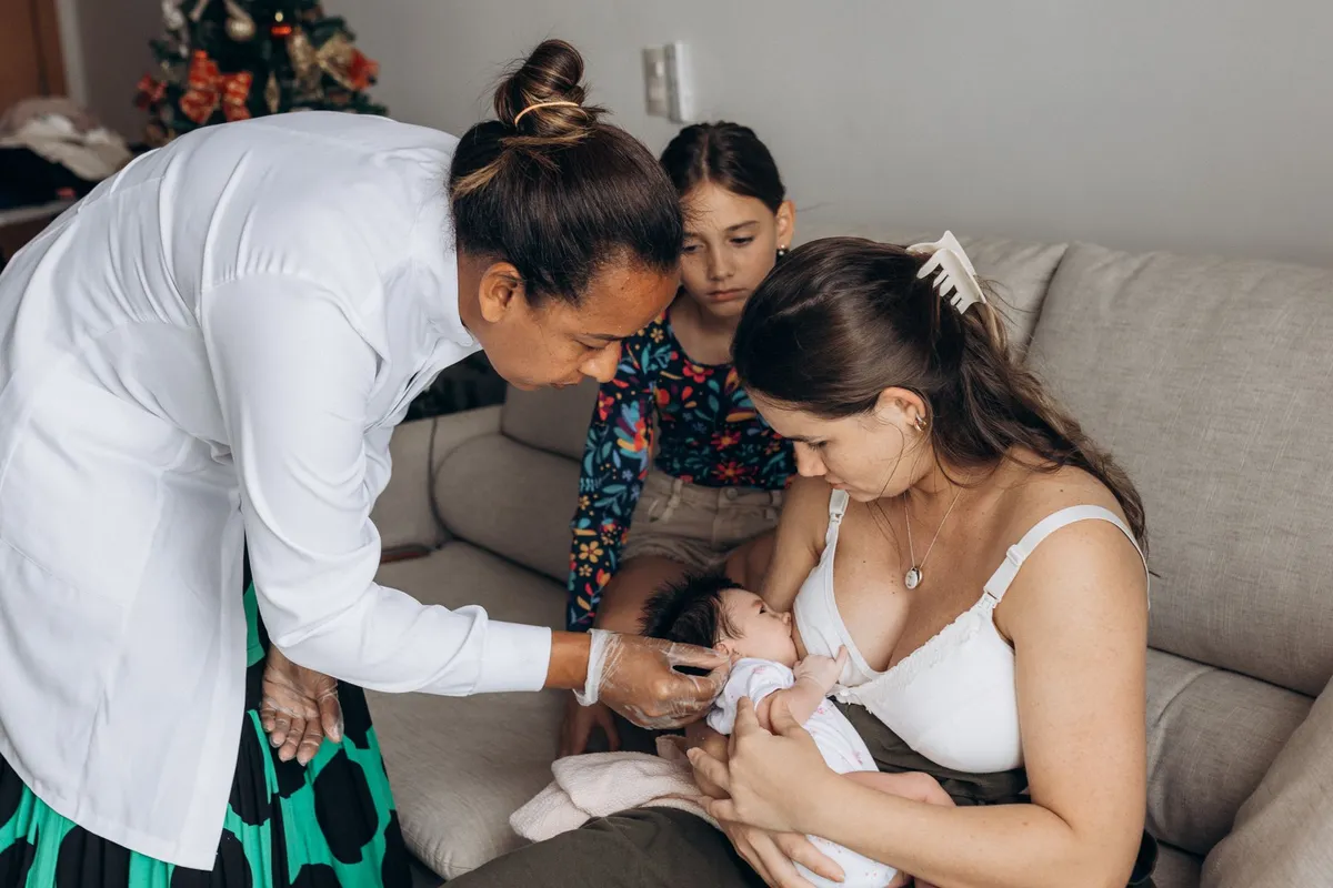 Mother breastfeeding her baby with a healthcare professional present.