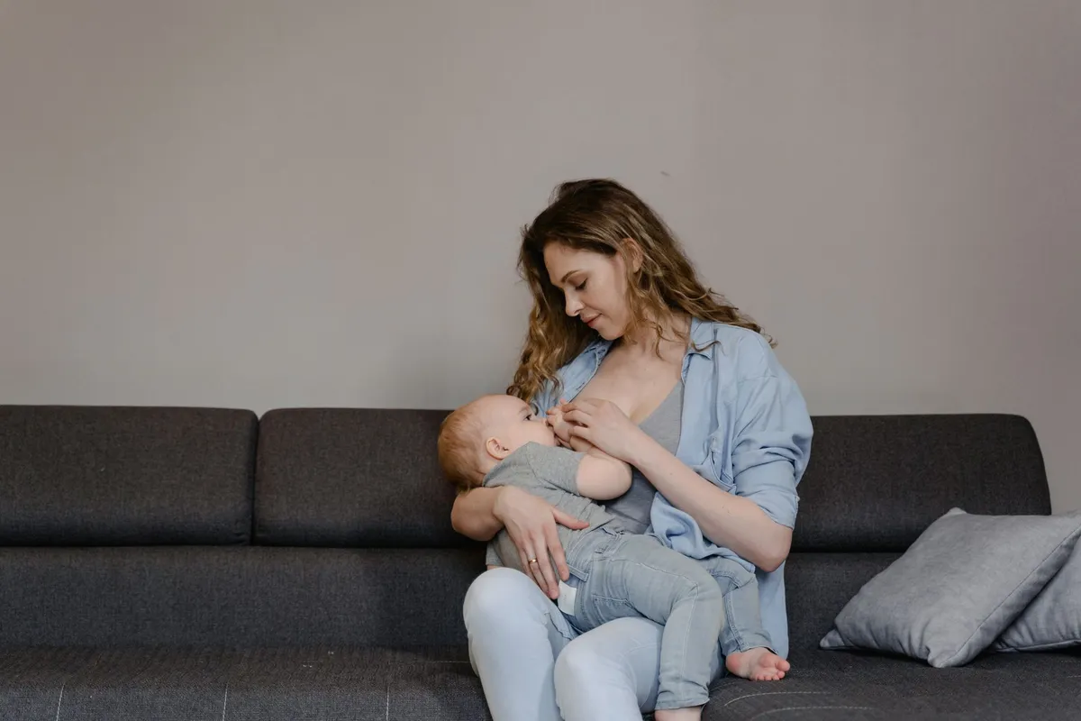 Mother breastfeeding her baby while sitting on a couch in a cozy setting.
