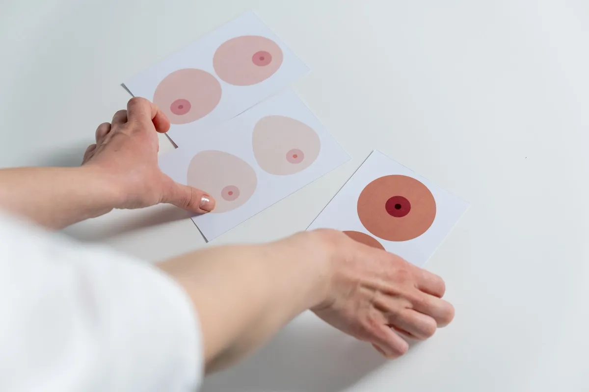 Hands arranging cards showing different breast shapes and colors.