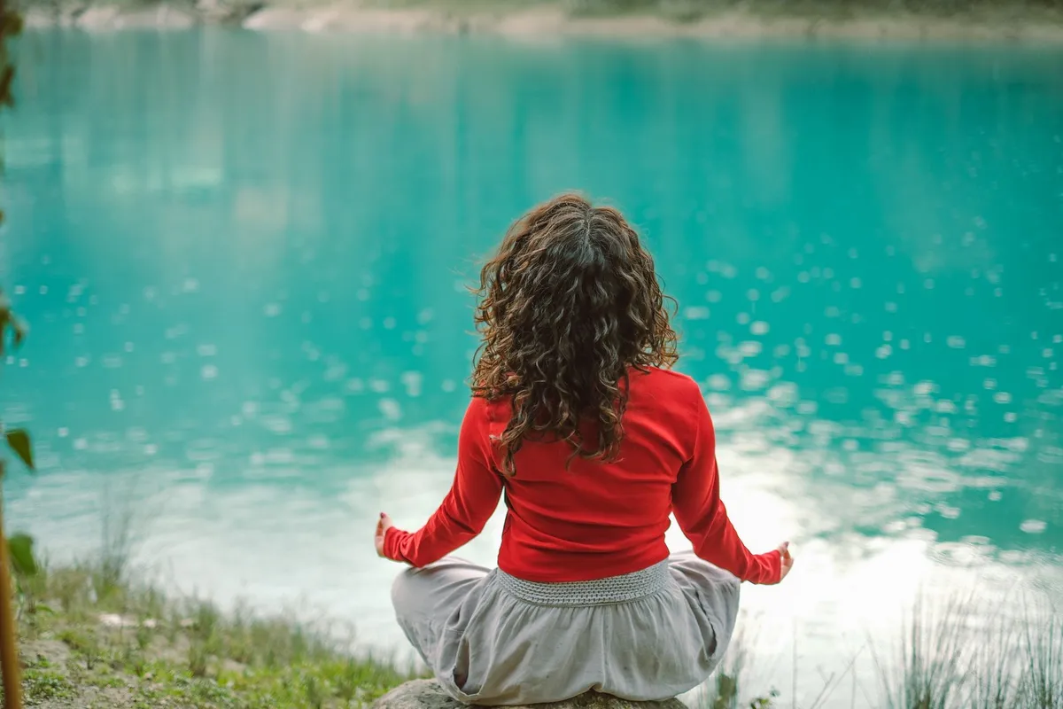 Woman meditating by a serene lake, promoting deep breathing and relaxation.