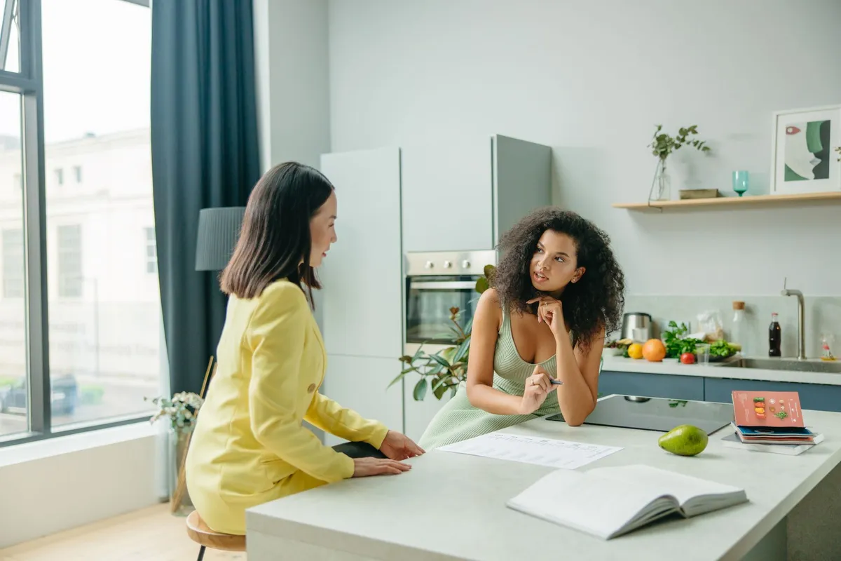Two women discussing nutrition in a modern kitchen setting with fruits visible.