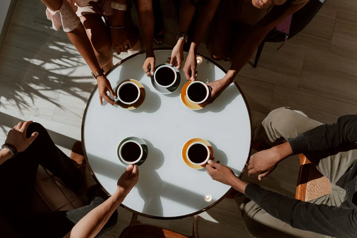 Group of friends holding coffee cups around a table in a coffee shop setting.