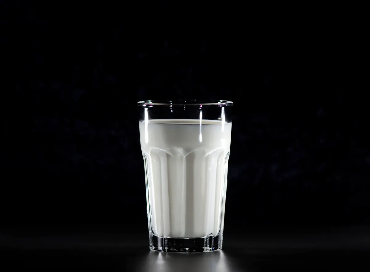 A clear glass filled with milk against a dark background.
