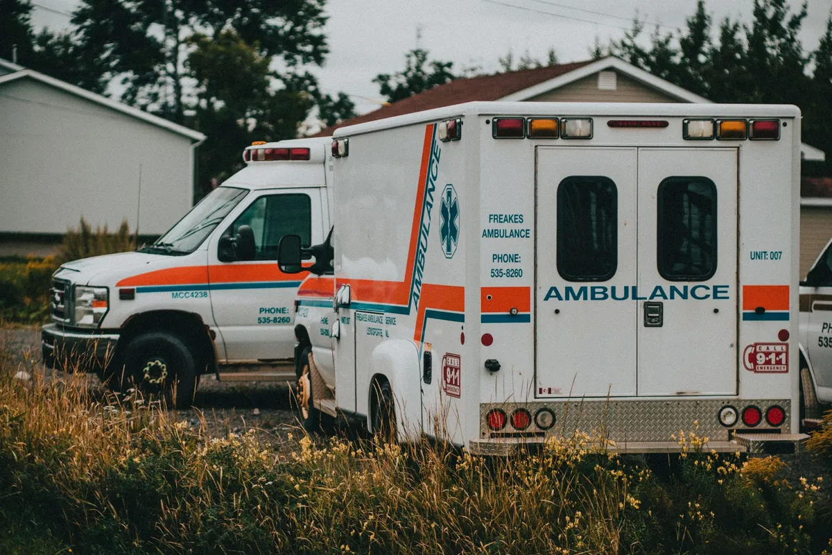Ambulance parked outside with emergency lights on, in a grassy area.