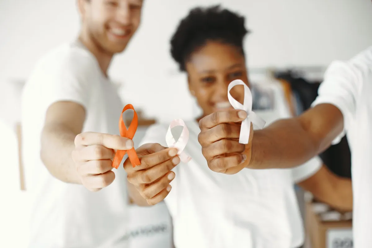 Three people holding cancer awareness ribbons in a supportive setting.