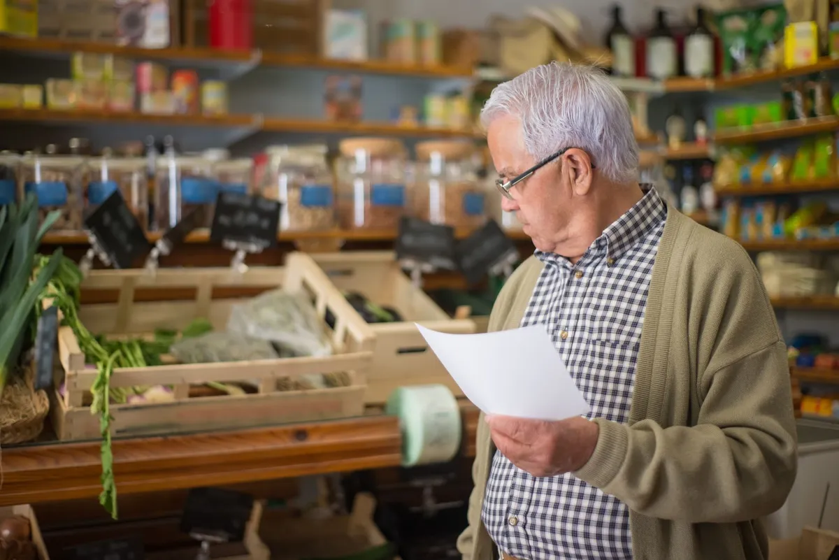 Older man reading a nutrition label while shopping in a grocery store.