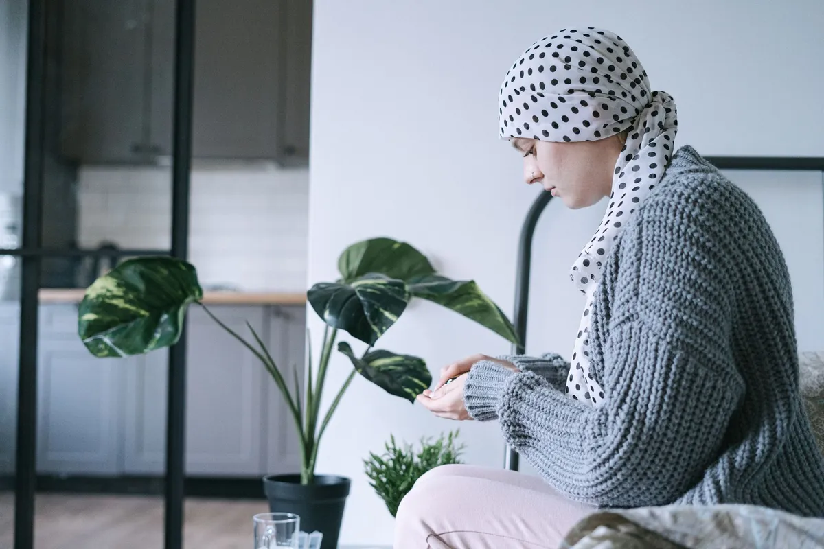 A woman with a headscarf sitting and holding pills, reflecting on her health.