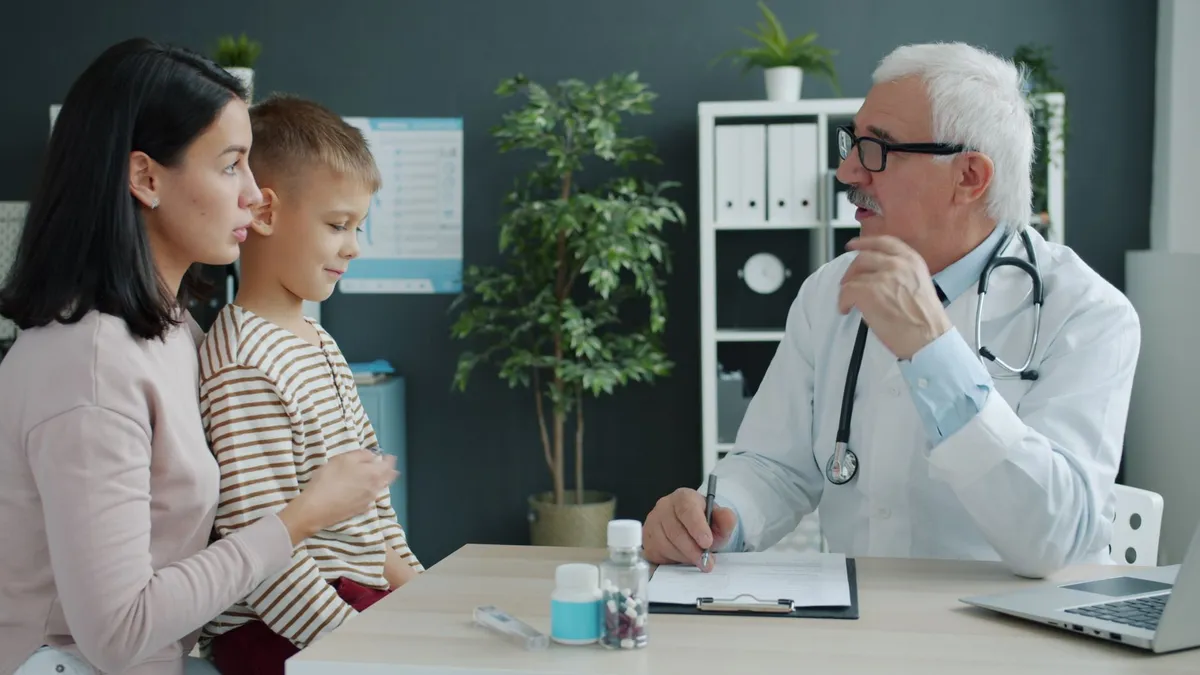 Pediatrician discussing health with a child and parent in a clinical setting.
