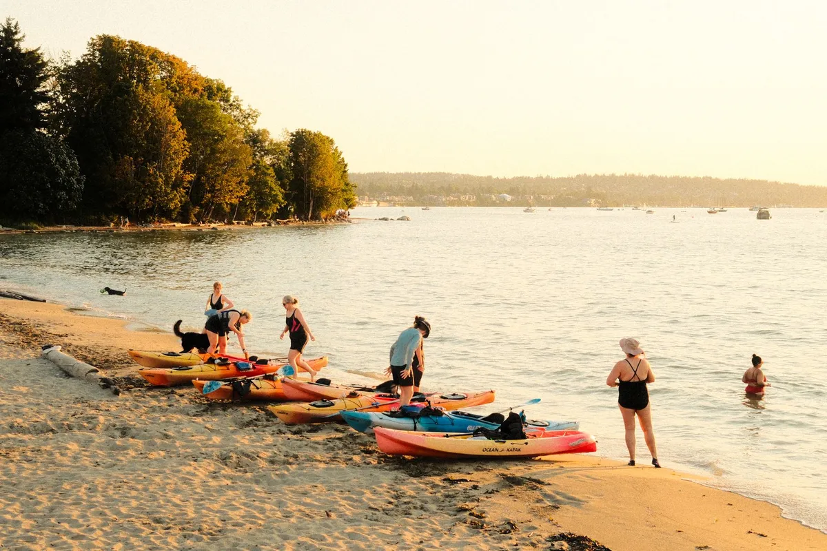 Group of people with kayaks on a sandy beach during sunset