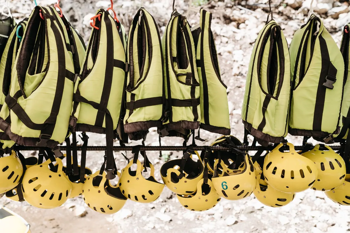 Yellow helmets and green life jackets hanging on a rack.