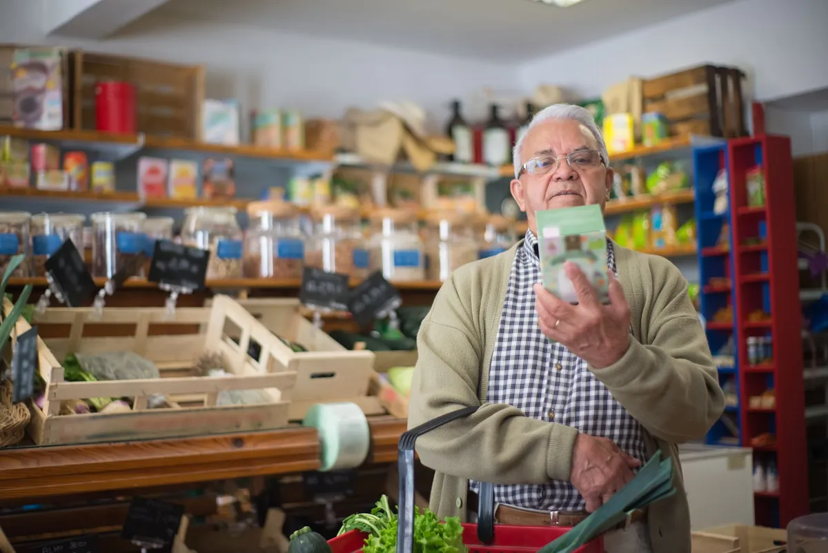 Older adult examining a food package in a grocery store aisle.