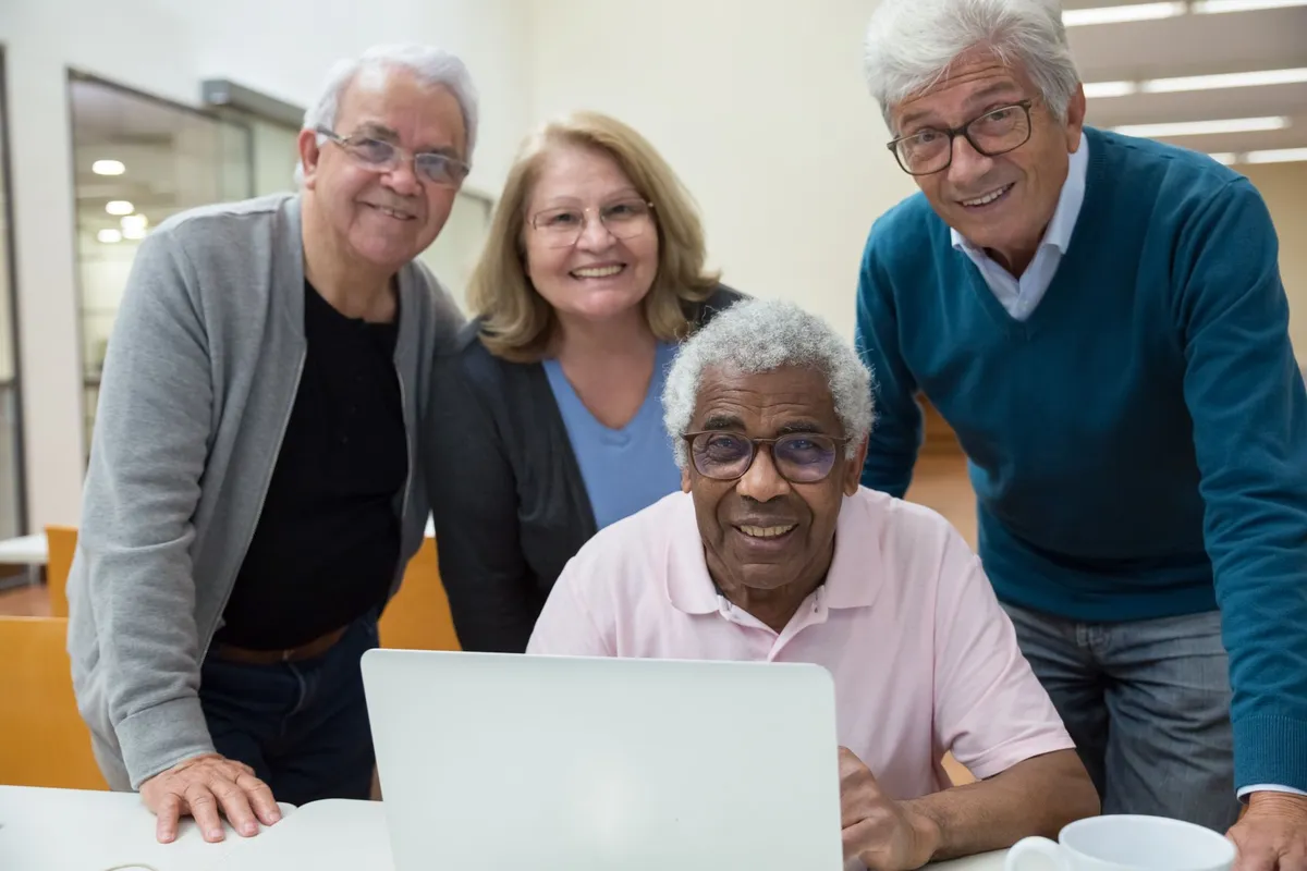 Four seniors smiling and engaging with a laptop in a casual setting.