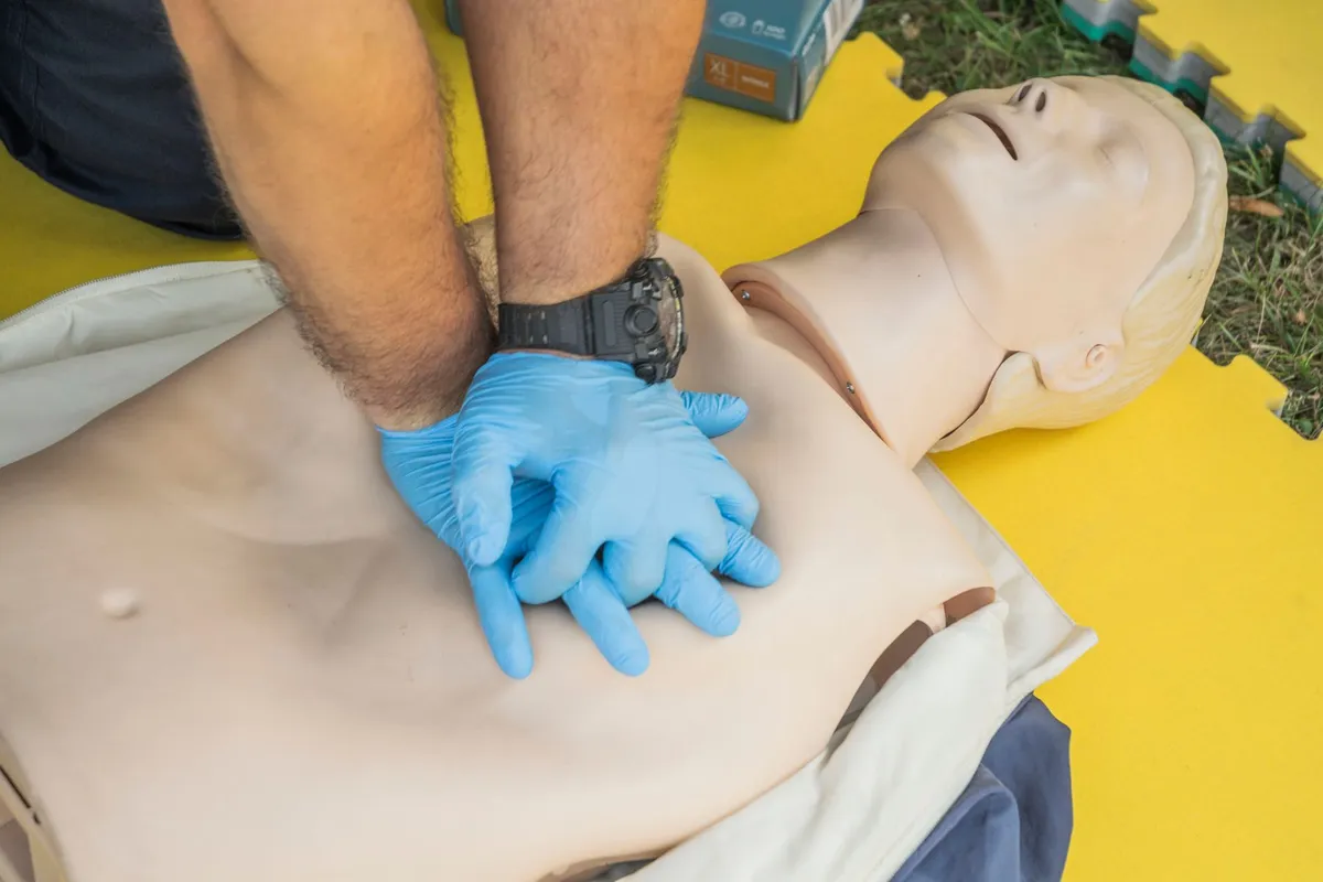 Hands performing chest compressions on a CPR training mannequin.