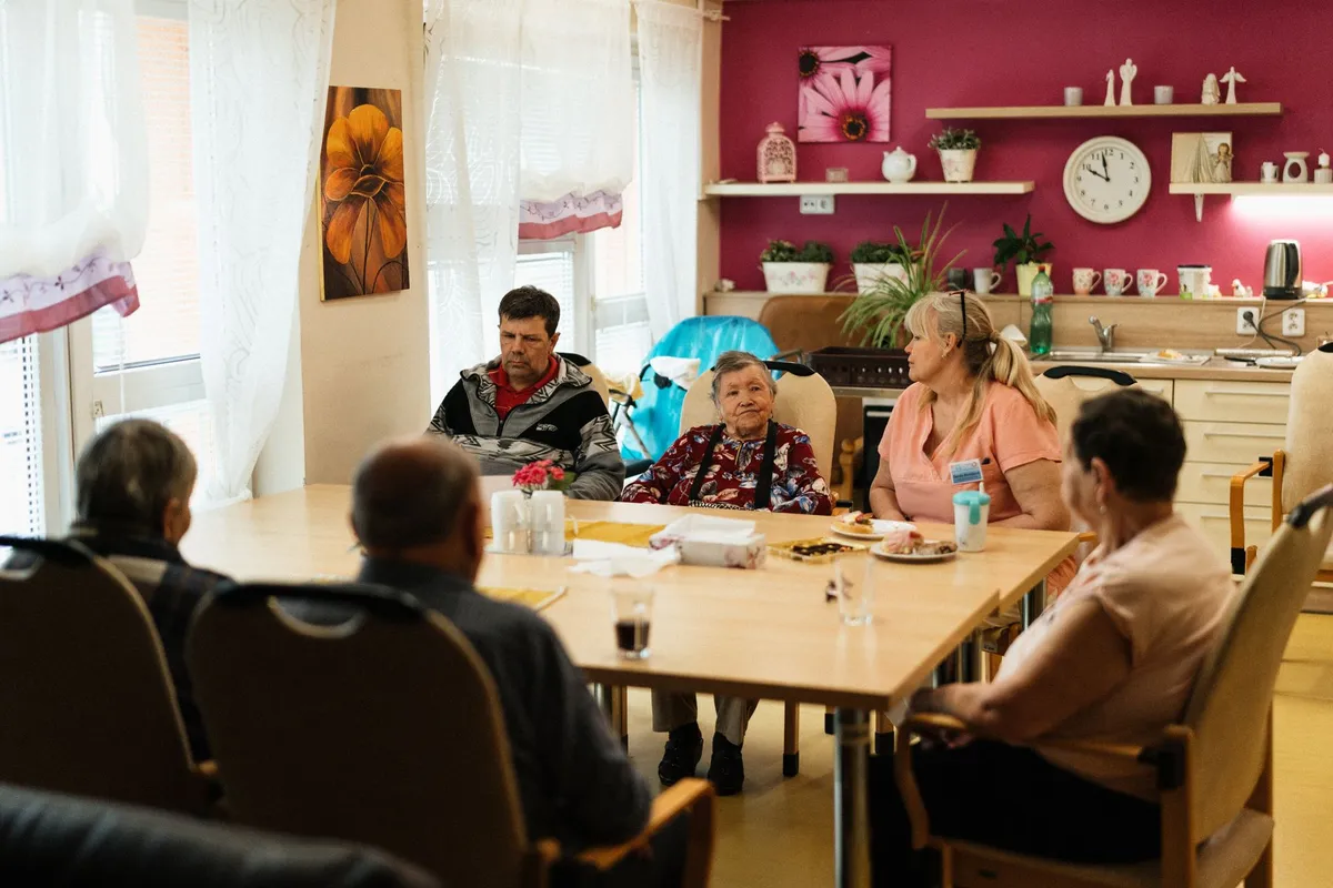 Group of caregivers and elderly individuals seated around a table in a community setting.