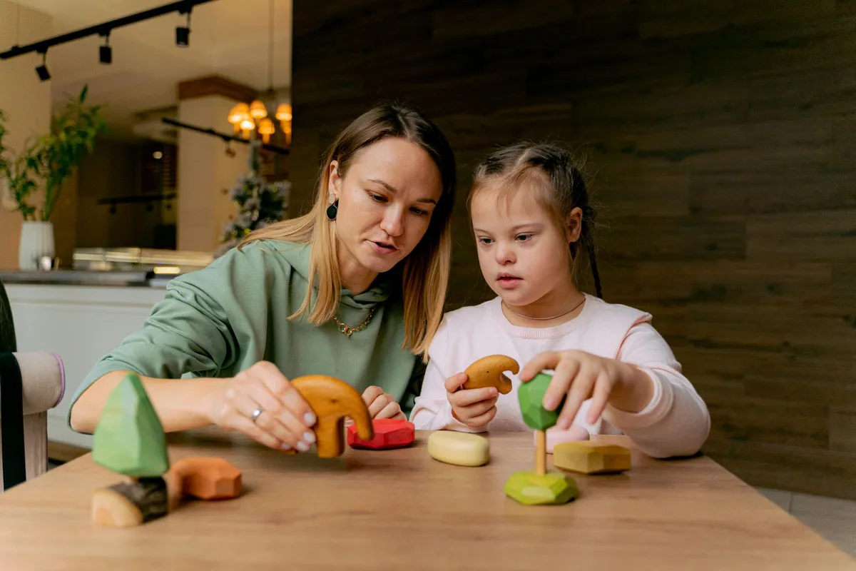 A caregiver and a child playing with wooden toys at a table in a cozy home setting.