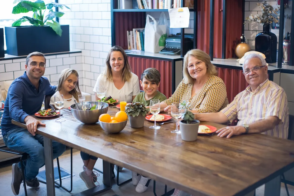 Family gathering around a table with food, including grandparents and children in a cozy setting.