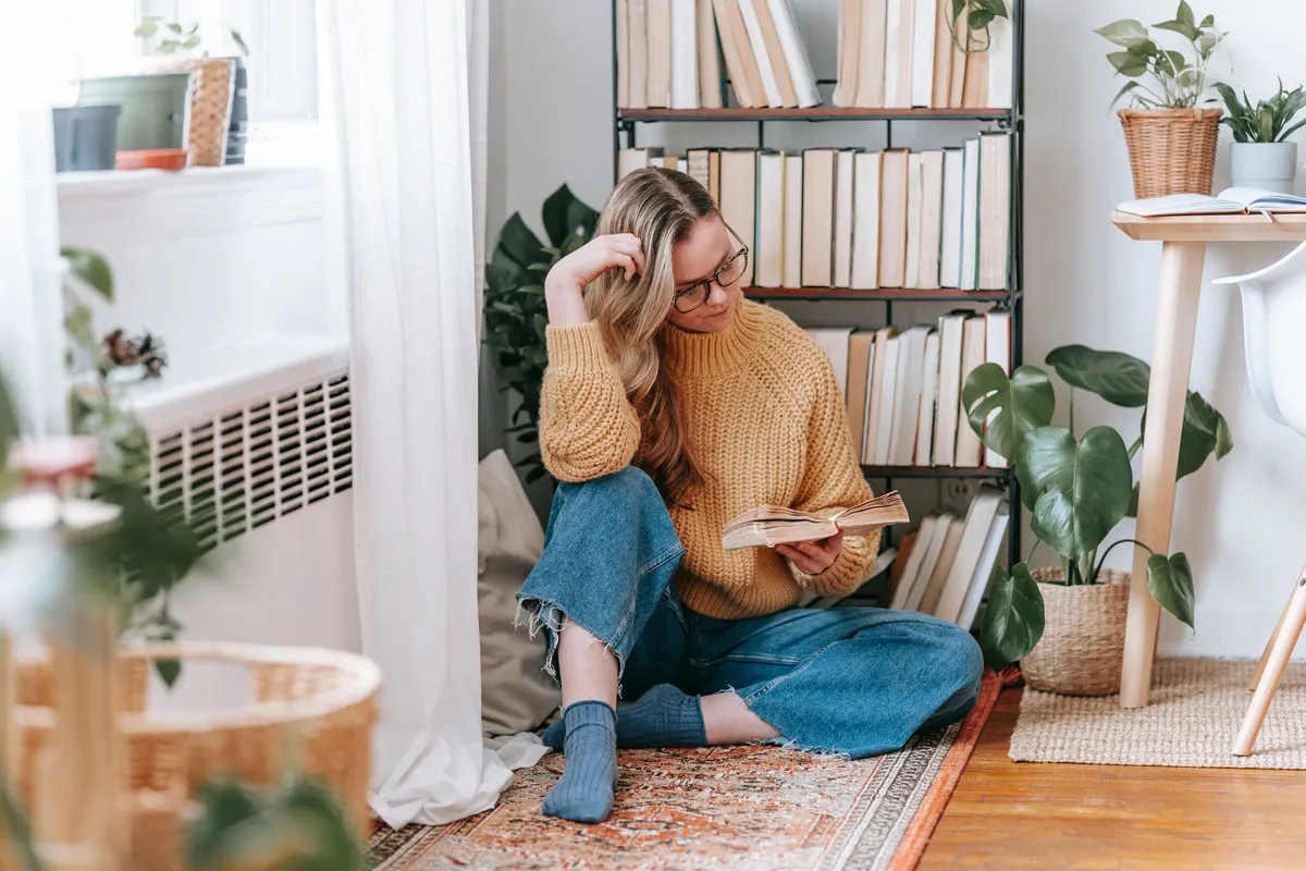 Person reading a book in a cozy, plant-filled corner of a room.