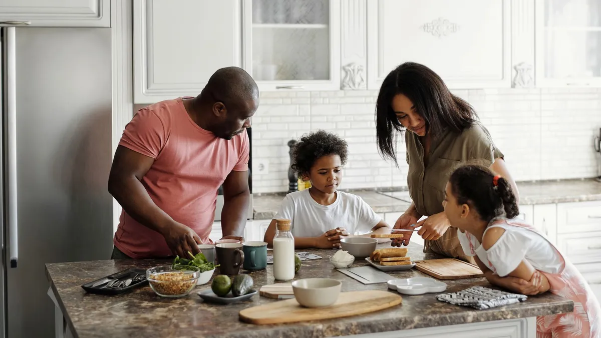 Family preparing breakfast with wholegrain foods and fruits in a kitchen.