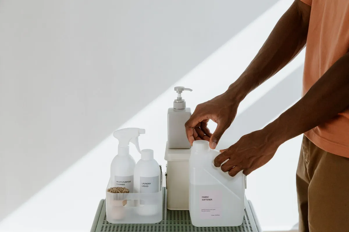 Person handling various household cleaning products on a table.